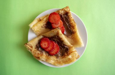 Çikolata ezmeli taze gözleme ve yeşil arka planda çilek. Krep Haftası için Rus usulü krep.. 