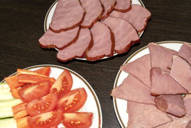 Smoked horse and beef meat slices on white plates on dark wooden background with fresh vegetables. Mixing meat delicacy, sirloin 
