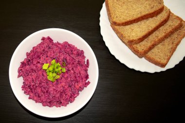 Koyu ahşap masada kahverengi ekmekli beyaz bir kasede leziz pancar salatası. Peynirli pancar, ekşi krema ve yeşil soğan, sağlıklı ve taze yemek.. 