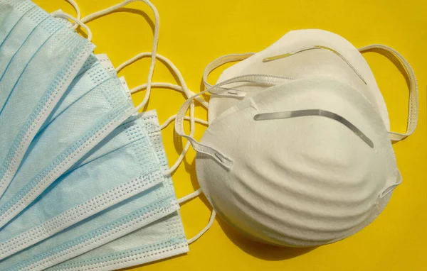 Different types of surgical disposable face masks on yellow background. Top view. Medical blue masks. PPE equipment on yellow. Face mask protection against dust, pollution and viruses.