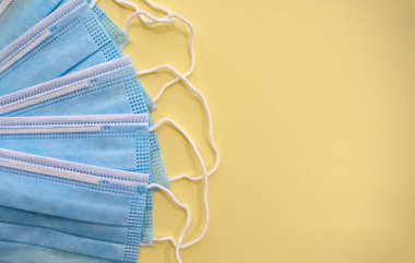 Sarı arka planda tek kullanımlık ameliyat maskeleri ve fotokopi alanı. Üst Manzara. Tıbbi mavi maskeler. Virüslere karşı önleyici önlem olarak tıbbi solunum bandajları. PPE ekipmanları sarıda izole edildi