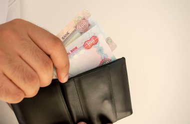 BAE ulusal para birimi. Para banknotları. Beyaz tişörtlü adam siyah cüzdana dirhem banknotları koymuş. Delikanlı cüzdanı elinde tutuyor. Fotokopi alanı olan kağıt paralarla. 