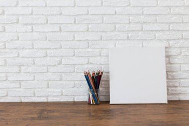 Boş beyaz tuval çerçeve ve renkli kalemler ahşap bir masa üzerinde