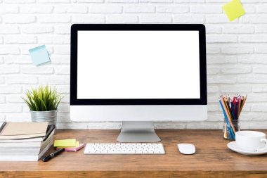 Boş beyaz ekranlı bilgisayar ve ahşap bir masada ofis malzemeleri olan çalışma alanı.