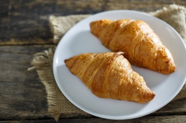 Beyaz tabakta kruvasan, ahşap bir masanın üstüne yerleştirilmiş.