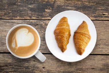 Kahveli kruvasan, beyaz tabakta, ahşap bir masanın üstüne yerleştirilmiş.