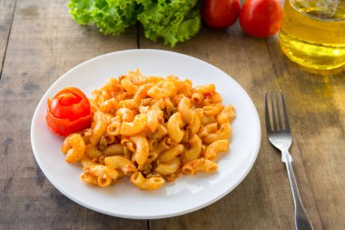 Yumurtalı, domuzlu ve sebzeli kızarmış makarna. Tabakta domates sosu, ahşap bir masaya konur.