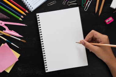 Kız el çizimi, renkli kalemli boş kağıt ve ahşap masadaki okul malzemeleri.