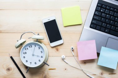 Alarm saati, yapışkan notları ve ahşap masa görünümlü bilgisayarı olan akıllı telefon..