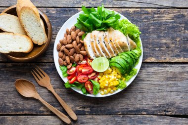 Sağlıklı yemek, sebze salatası, tavuk ve badem, ahşap bir masada beyaz bir tabakta. Üst görünüm