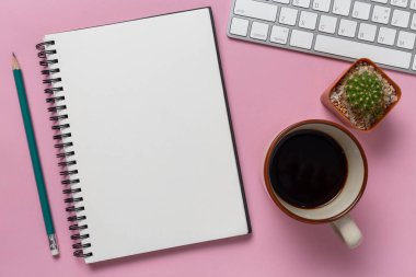 Üst görünüm, boş defter ve ofis malzemeleri pembe arka planda.