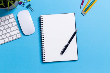 Üst görünüm, boş defter ve ofis malzemeleri mavi masada..