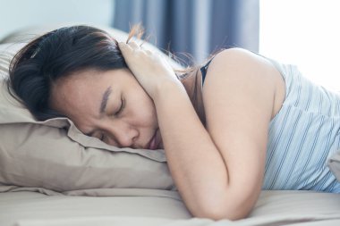 Yatakta yatan genç bir kadın yastıkla başını ve kulaklarını kaplayan sesten muzdarip ve tatsız bir yüz ifadesi takınıyor. Erken kalktım. Yeterince uyuyamadım.