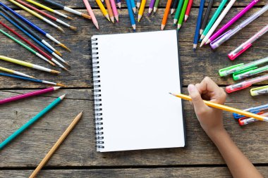 Kız eli çizimi, boş kağıt ve ahşap masa üzerinde renkli kalemler.