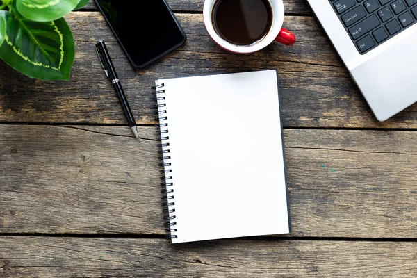 Akıllı telefonu ve bilgisayarı ahşap masa üstünde olan boş bir defter.