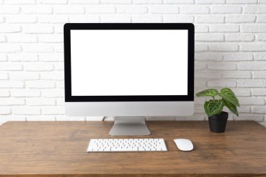 Boş beyaz ekranlı bilgisayar ve ahşap bir masada ofis malzemeleri olan çalışma alanı.