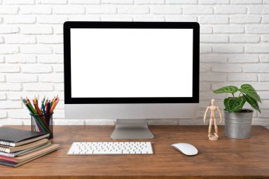Boş beyaz ekranlı bilgisayar ve ahşap bir masada ofis malzemeleri olan çalışma alanı.