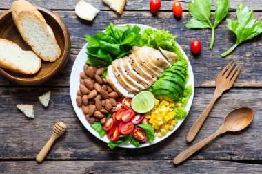 Sağlıklı yemek, sebze salatası, tavuk ve badem, ahşap bir masada beyaz bir tabakta. Üst görünüm