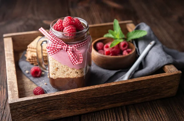 No-bake layered dessert with dark chocolate mousse, crushed cookies and raspberry cream cheese in glass jar — Stock Photo, Image