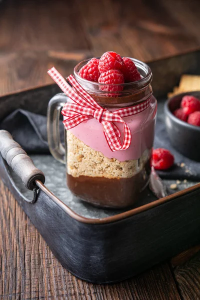 No-bake layered dessert with dark chocolate mousse, crushed cookies and raspberry cream cheese in glass jar — Stock Photo, Image