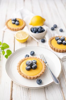 Limon kaymaklı ceviz kabuklu tart, üzerine taze yaban mersini serpiştirilmiş ve pudra şekerli.