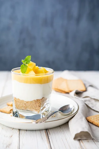 Sweet layered dessert with crushed graham crackers, cream cheese and pineapple curd, topped with fresh fruit slices in a glass jar — Stock Photo, Image