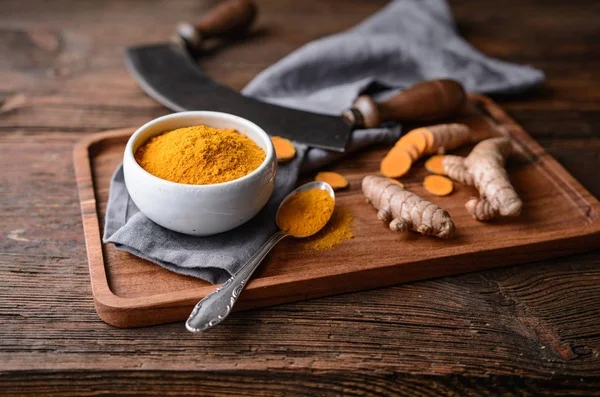 Ingrediente alimentare antinfiammatorio, curcuma in polvere in una ciotola di ceramica e radice fresca su fondo di legno — Foto Stock