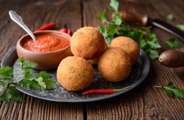 Ev yapımı klasik Arancini Di Riso, Mozzarella peyniri ile doldurulmuş gevrek Sicilya pirinç topları, kırsal ahşap arka planda sıcak Arrabbiata sosu ile servis ediliyor.