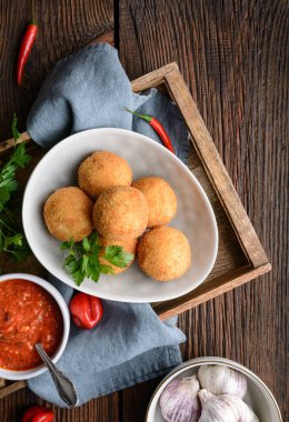 Ev yapımı klasik Arancini Di Riso, Mozzarella peyniri ile doldurulmuş gevrek Sicilya pirinç topları, kırsal ahşap arka planda sıcak Arrabbiata sosu ile servis ediliyor.