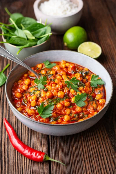 Indian meal, spicy chickpea curry with spinach in a bowl served with rice on rustic wooden background