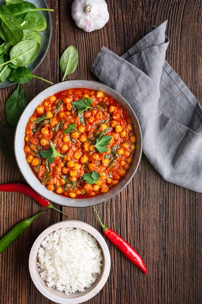 Indian meal, spicy chickpea curry with spinach in a bowl served with rice on rustic wooden background
