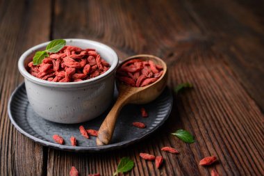Bağışıklığı arttırmak için bol miktarda antioksidan ve vitamin içeren sağlıklı atıştırmalıklar, kabın içinde kurutulmuş Goji üzümü ve kopyalanmış ahşap arka planda bir kepçe dolusu fotokopi alanı