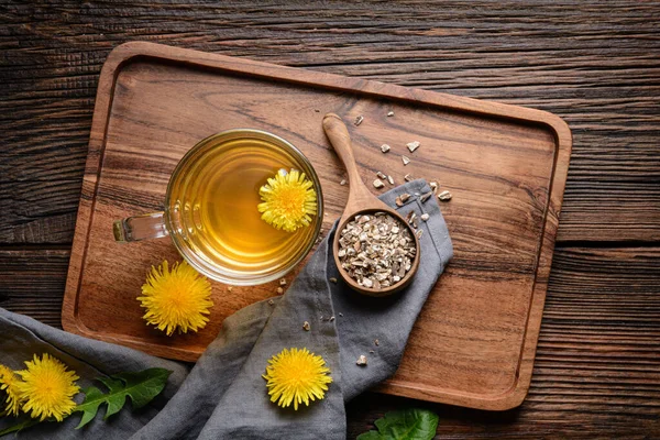 Herbal drink for liver detox, dandelion root tea in a glass cup decorated with fresh flowers on a rustic wooden background