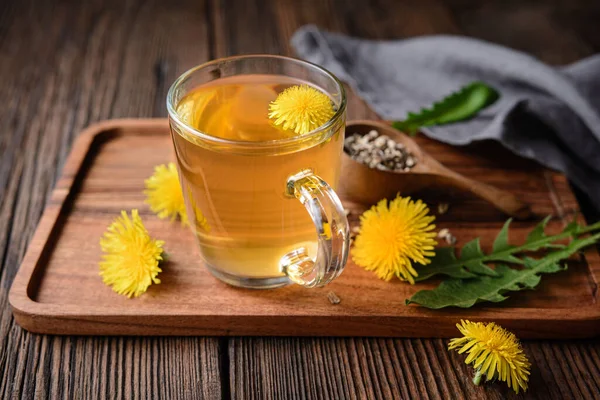 Herbal drink for liver detox, dandelion root tea in a glass cup decorated with fresh flowers on a rustic wooden background