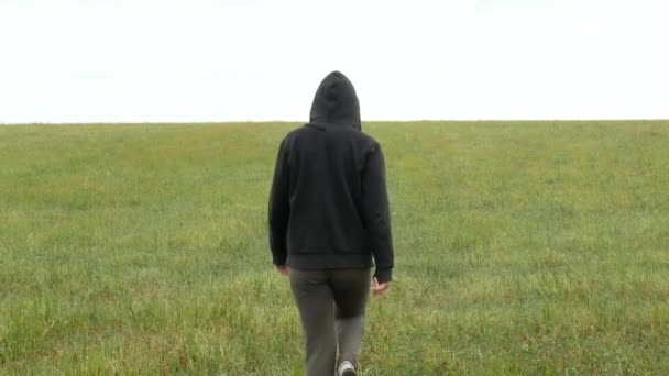 Chica en traje deportivo caqui y capucha camina a través de un prado — Vídeos de Stock