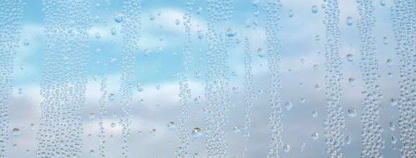 Drops water on window for wallpaper design. Blue cloudy sky backdrop. Spotted abstract texture background. Spring wet weather panorama. Droplets on glass in horizontal natural cover. Fit to autumn
