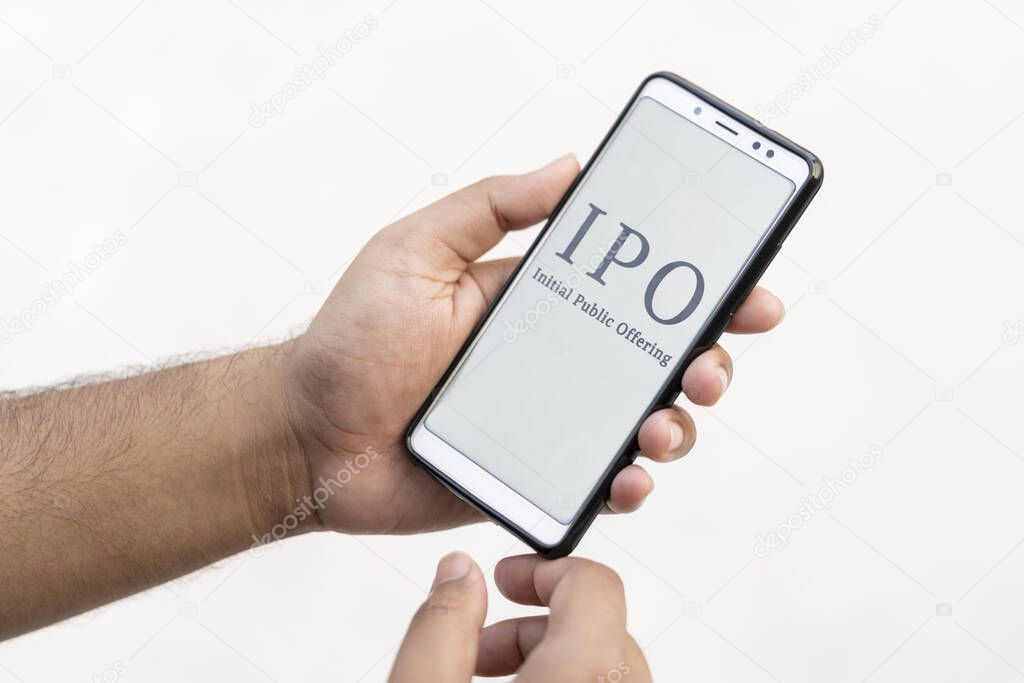 IPO concept. Indian working man hand holding smart phone & showing Initial Public Offering which is displayed on it's screen isolated on white background with copy space.