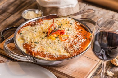 Peynirli ve domates soslu lezzetli ev yapımı lazanya ahşap arka planda ve kırmızı şarap.