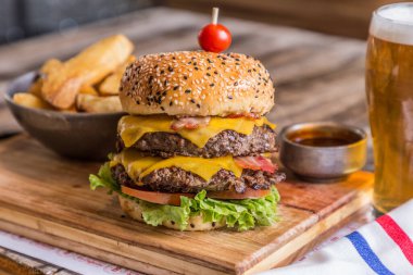 Patates kızartması, marul, domates, peynir, salatalık turşusu ve kızarmış patates, beyaz sos ve ketçap ile servis edilen kırmızı soğanlı ev yapımı iştah açıcı hamburger. Bira bardağıyla.