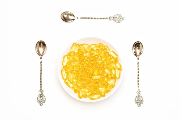 Ortadaki beyaz bir tabakta her iki tarafında üç kaşık olan bir sürü Omega 3 vitamini. Yukarıdan görüntüle.