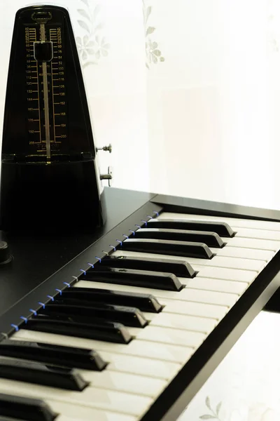 Metronoom boven de piano verlicht door het licht door het gordijn, natuurlijke witte achtergrond, selectieve focus, muziekconcept — Stockfoto