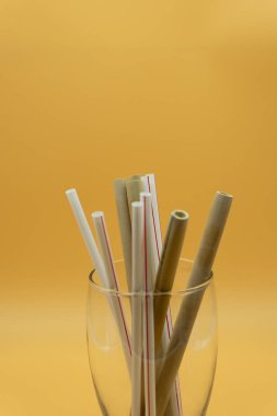Sarı arka plandaki bir bardağın içinde plastik ve bambu pipetlerinin görüntüsü. Sıfır atık.