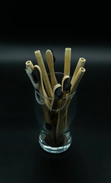 Top view of a bamboo toothbrushes and bamboo straws inside a glass on a black background. Zero waste concept.