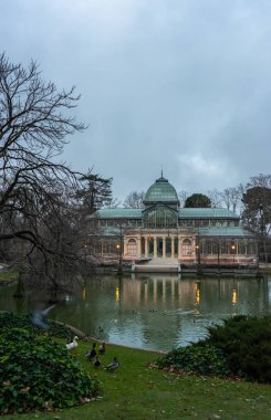 Madrid 'deki Etiro Parkı' nda, bulutlu bir günde cam sarayın yanında gün doğumunun dikey görüntüsü. Seyahat kavramı.