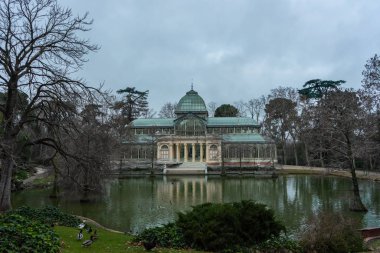 Madrid, Retiro Park 'taki cam sarayın manzarası, şafak vakti bulutlu bir günde, çimlerin üzerinde yürüyen ördekler, seyahat konsepti.
