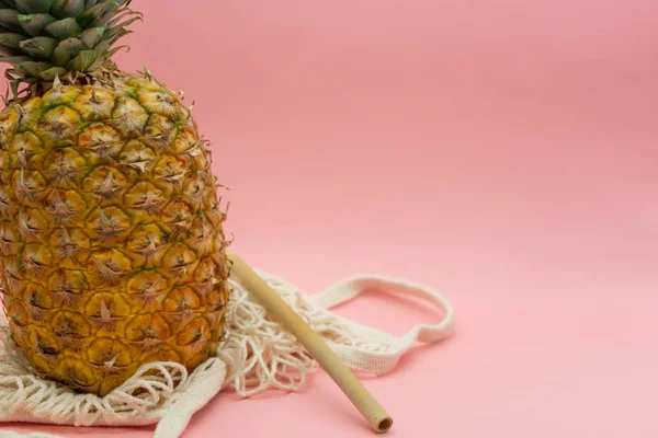 Piña con bolsa de algodón orgánico y paja de bambú aislada sobre fondo rosa, situada a la izquierda de la imagen con espacio para texto a la derecha. Concepto alimentario saludable y ecológico. Residuos cero . — Foto de Stock