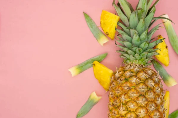 Abacaxi inteiro com pedaços e folhas ao redor, isolado em um fundo rosa. Espaço à esquerda. Conceito alimentar saudável e ecológico . — Fotografia de Stock