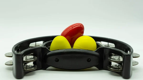 Black tambourine with eggs shakers on top on a white background with space at the top of the image. Concept percussion instruments.