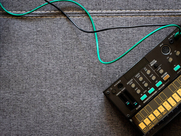 Top view of small black fm synthesizer with patch cables on top of a sofa with space to the left of the image. Electronic music concept