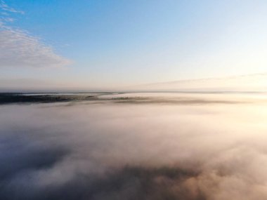 Şafak vakti bulutların üzerinde sis ile uçan insansız hava aracının görüntüsü.